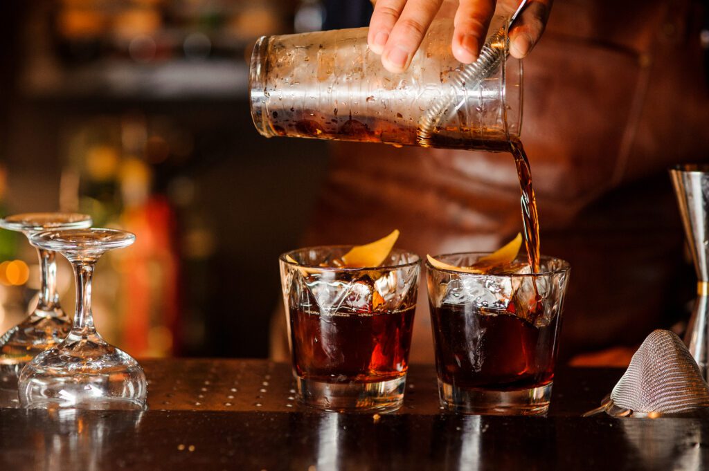 Bartender pouring fresh alcoholic drink into the glasses with ice cubes
